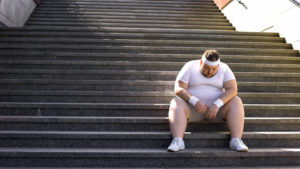 Sliten overvektig man sitter i trappen i treningstøy